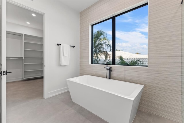 full bath with a soaking tub, recessed lighting, concrete flooring, and baseboards