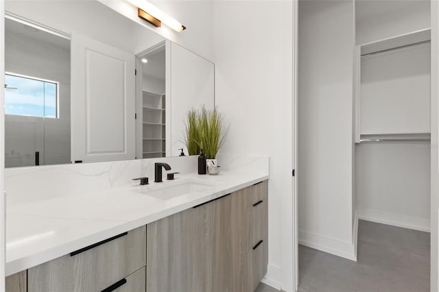 bathroom with baseboards, vanity, and a spacious closet