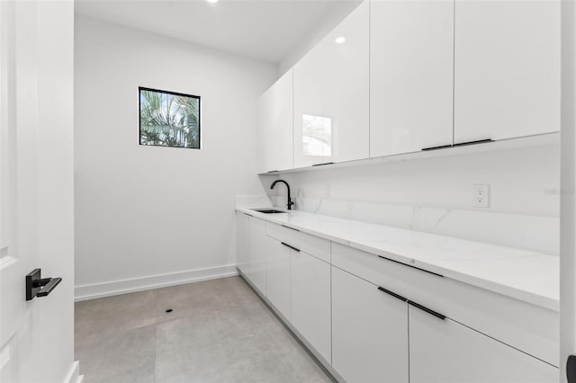 interior space with modern cabinets, light stone counters, a sink, white cabinetry, and baseboards