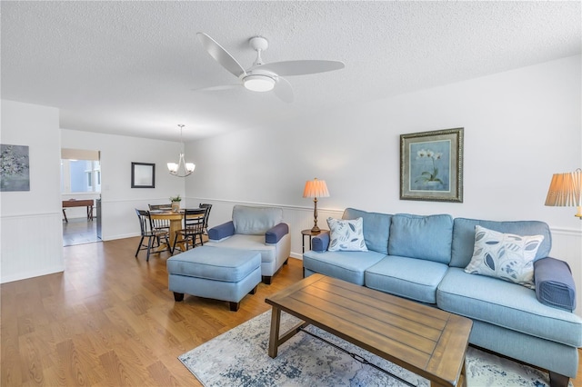 living room with wood-type flooring, ceiling fan with notable chandelier, and a textured ceiling