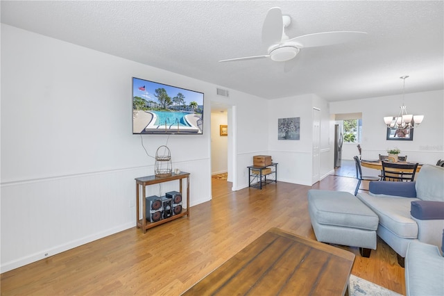 living room with hardwood / wood-style flooring, ceiling fan with notable chandelier, and a textured ceiling