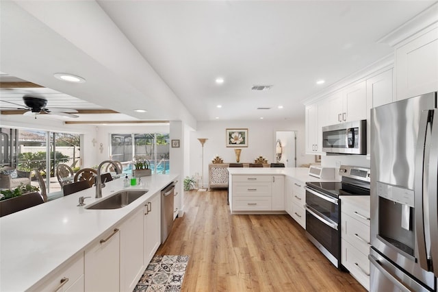 kitchen with stainless steel appliances, light countertops, visible vents, a sink, and a peninsula