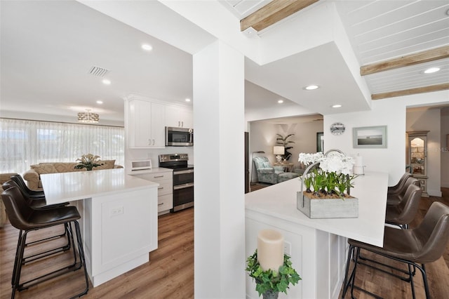 kitchen with white cabinets, a breakfast bar, open floor plan, stainless steel appliances, and light wood-type flooring