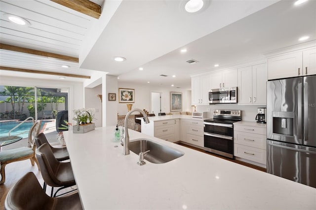 kitchen with recessed lighting, light countertops, appliances with stainless steel finishes, a sink, and a kitchen bar