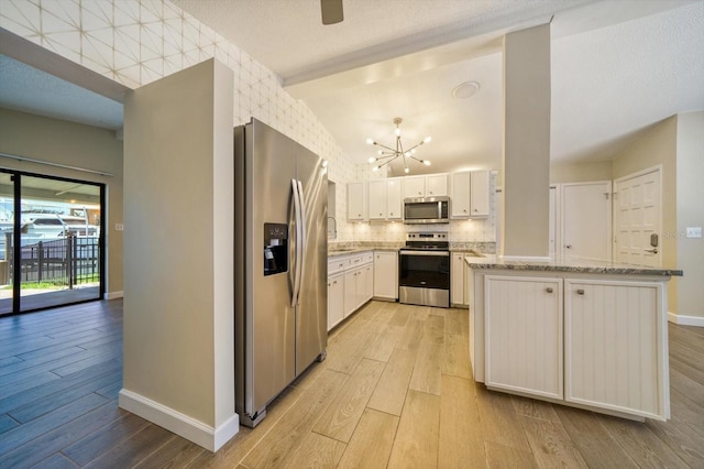 kitchen featuring white cabinets, light stone counters, stainless steel appliances, and light hardwood / wood-style floors