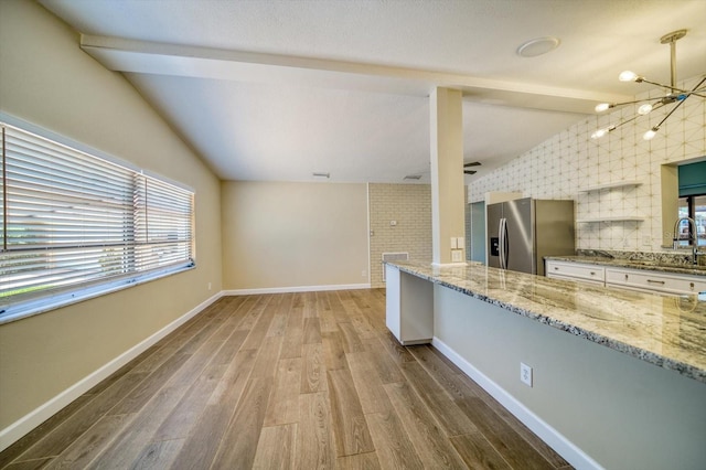 kitchen featuring light stone countertops, an inviting chandelier, vaulted ceiling with beams, stainless steel fridge, and hardwood / wood-style flooring