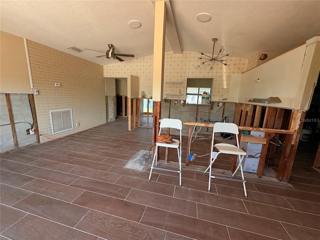 interior space with brick wall, ceiling fan with notable chandelier, vaulted ceiling with beams, and a textured ceiling