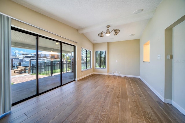 unfurnished room featuring wood-type flooring, vaulted ceiling with beams, a textured ceiling, and a healthy amount of sunlight