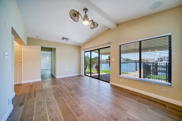 empty room featuring hardwood / wood-style floors, a water view, lofted ceiling with beams, and a textured ceiling