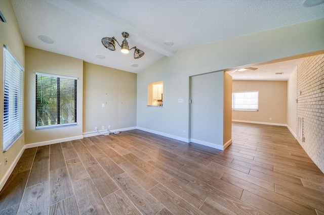 spare room with brick wall, vaulted ceiling with beams, wood-type flooring, and a textured ceiling