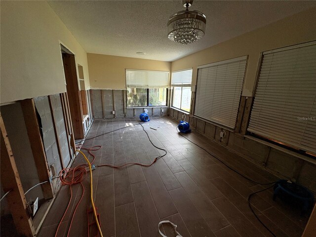 unfurnished room with a chandelier, dark wood-type flooring, and a textured ceiling