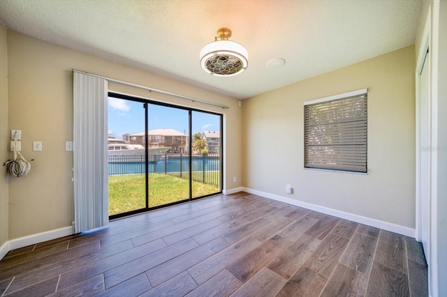 empty room with a textured ceiling, hardwood / wood-style flooring, and a water view