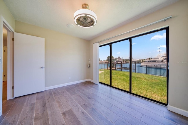 unfurnished room with a water view, light hardwood / wood-style floors, and a textured ceiling