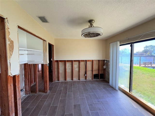 unfurnished room featuring a water view, a wealth of natural light, dark hardwood / wood-style flooring, and a textured ceiling