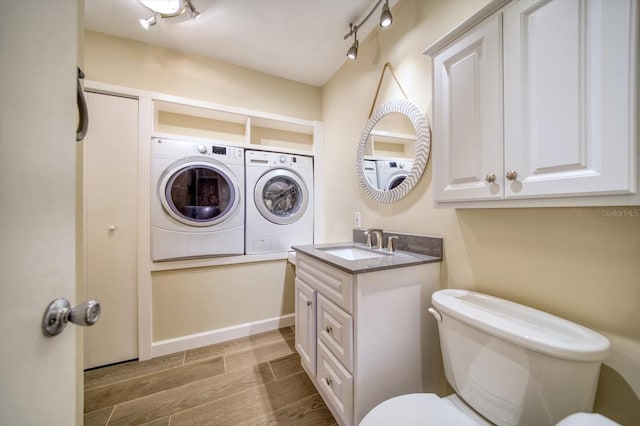 bathroom featuring rail lighting, toilet, vanity, washer and dryer, and hardwood / wood-style flooring