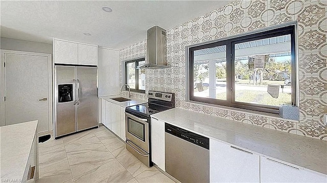 kitchen with stainless steel appliances, wall chimney exhaust hood, white cabinets, and plenty of natural light