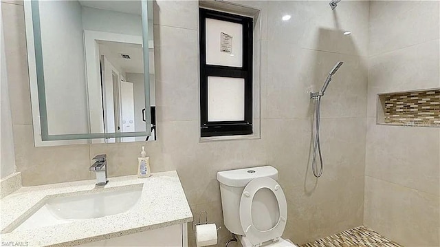 bathroom with tile walls, vanity, toilet, and a tile shower