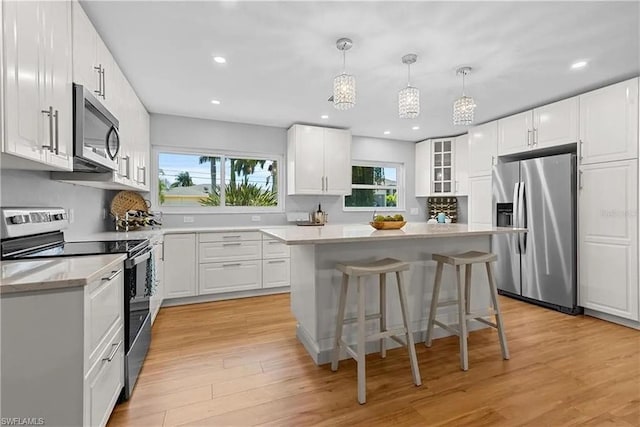 kitchen with stainless steel appliances, pendant lighting, a kitchen island, white cabinetry, and light wood-type flooring