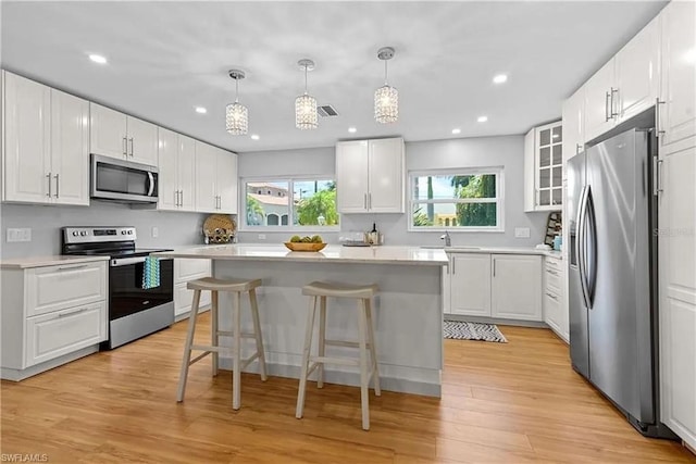 kitchen with white cabinets, a wealth of natural light, stainless steel appliances, and light hardwood / wood-style floors