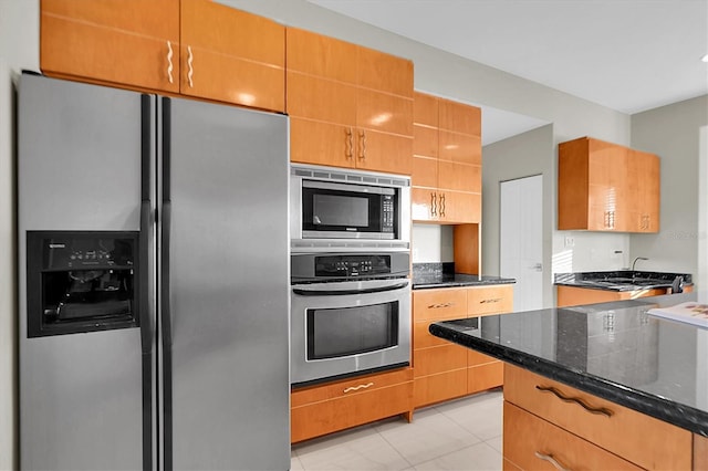 kitchen with light tile patterned floors, stainless steel appliances, and dark stone countertops