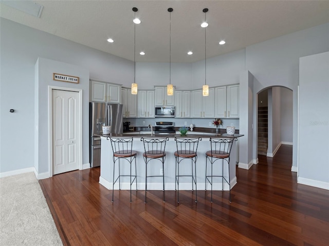 kitchen featuring dark wood-type flooring, a center island with sink, hanging light fixtures, gray cabinetry, and appliances with stainless steel finishes