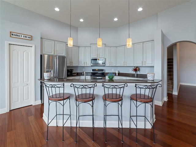 kitchen with dark hardwood / wood-style flooring, pendant lighting, a kitchen island with sink, and stainless steel appliances