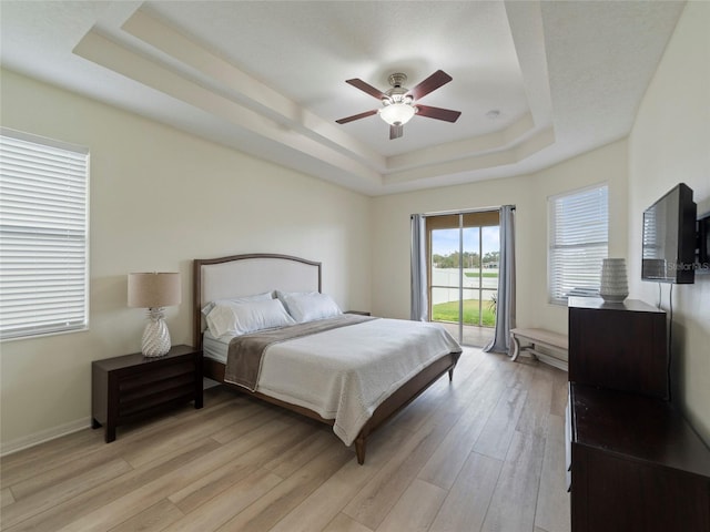 bedroom with ceiling fan, light hardwood / wood-style flooring, and a tray ceiling