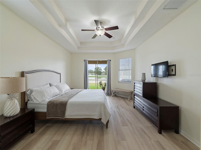 bedroom with light wood-type flooring, ceiling fan, and a raised ceiling