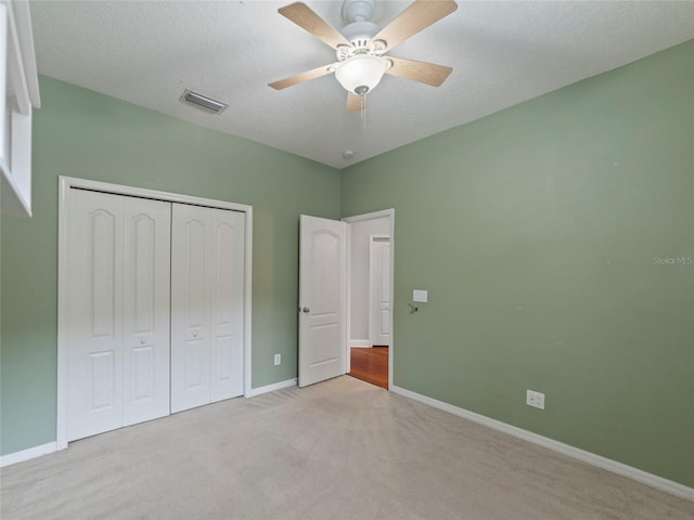 unfurnished bedroom featuring ceiling fan, light colored carpet, a textured ceiling, and a closet