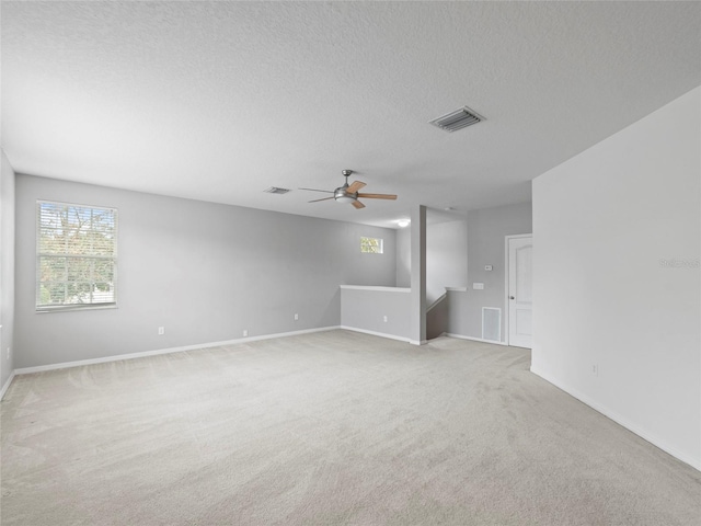 spare room with a textured ceiling, light colored carpet, and ceiling fan