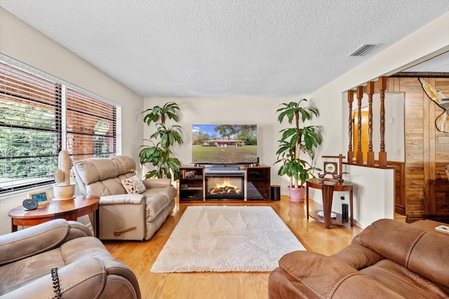 living room featuring light wood-type flooring, a textured ceiling, and wooden walls