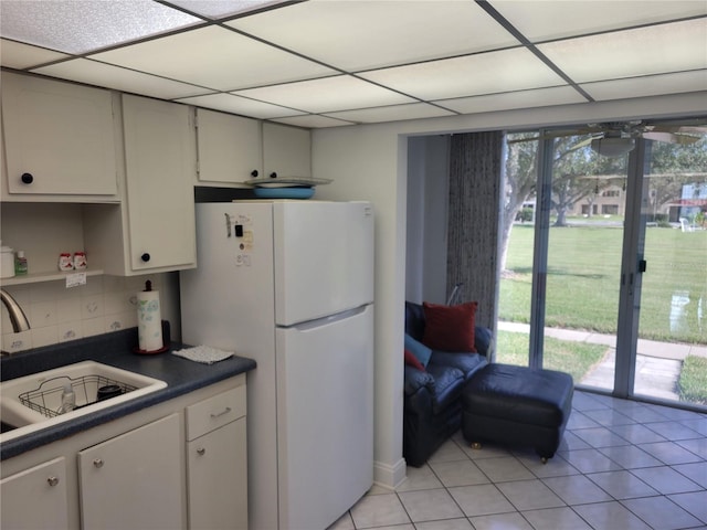 kitchen with white refrigerator, sink, a drop ceiling, and white cabinets