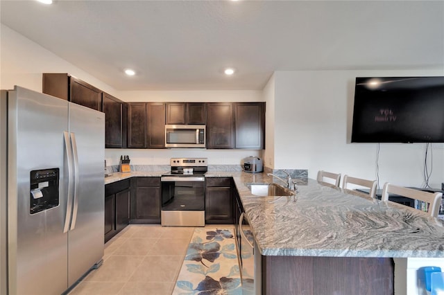 kitchen with stainless steel appliances, kitchen peninsula, sink, light stone countertops, and dark brown cabinets