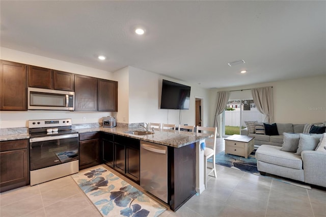 kitchen with stainless steel appliances, dark brown cabinetry, sink, kitchen peninsula, and light stone countertops