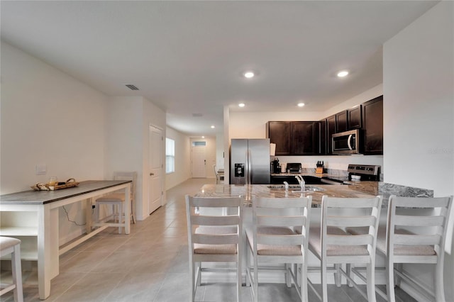 kitchen featuring kitchen peninsula, appliances with stainless steel finishes, dark brown cabinets, and a kitchen bar