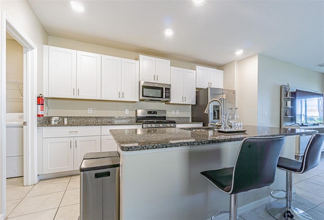 kitchen featuring white cabinets, stainless steel appliances, a breakfast bar area, and an island with sink