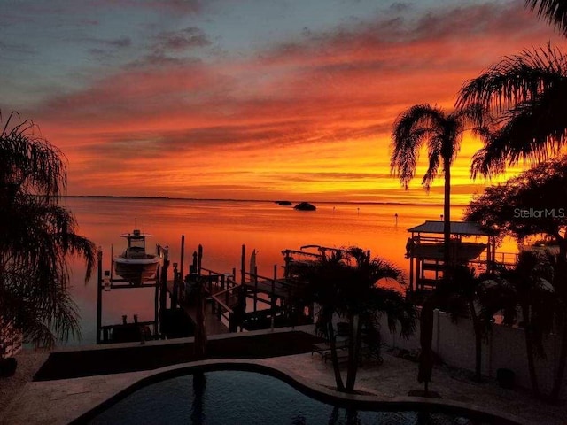 pool at dusk featuring a boat dock and a water view