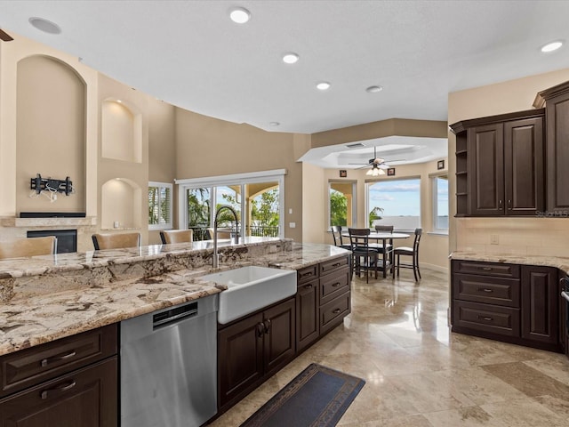 kitchen featuring dark brown cabinetry, ceiling fan, dishwasher, light stone countertops, and sink