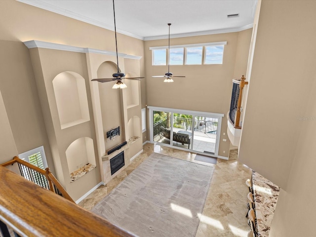 living room with ceiling fan, crown molding, and a tiled fireplace