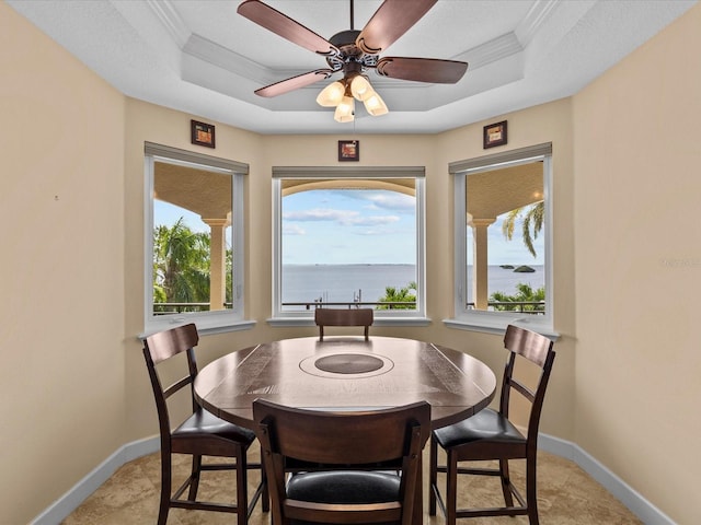 dining area with ornamental molding, a water view, plenty of natural light, and a tray ceiling