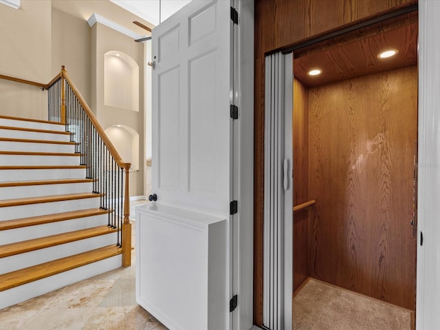 stairs featuring wooden walls, elevator, and ornamental molding