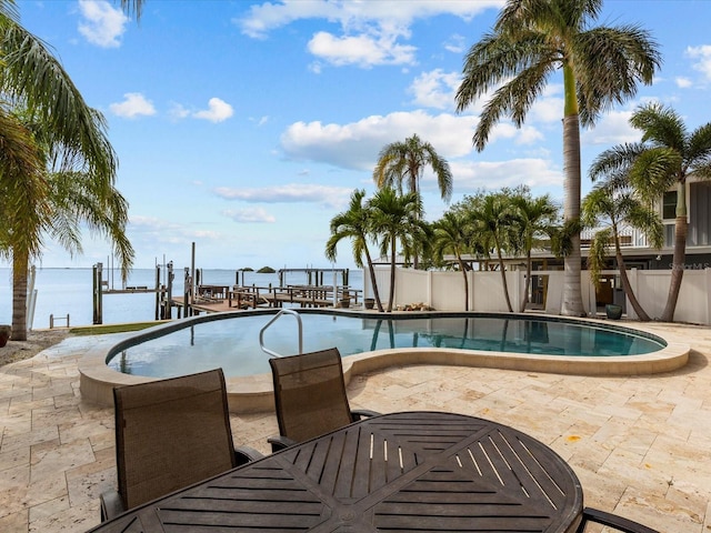 view of swimming pool with a dock, a water view, and a patio