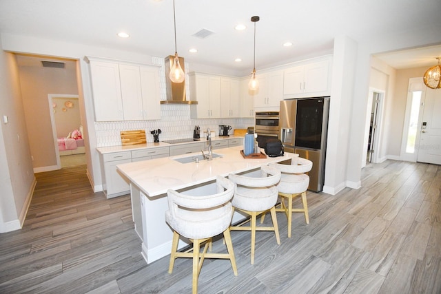 kitchen featuring a center island with sink, white cabinetry, sink, appliances with stainless steel finishes, and a breakfast bar area