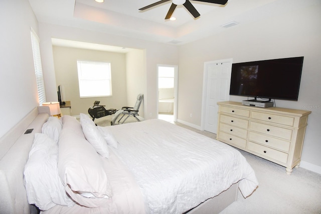 carpeted bedroom with connected bathroom, a tray ceiling, and ceiling fan