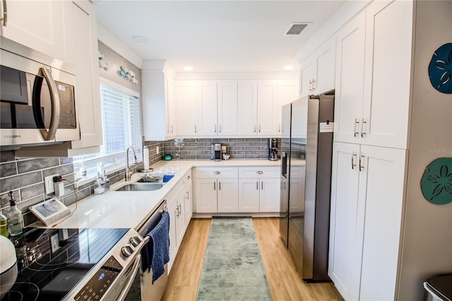130 63rd St S, Saint Petersburg, FL 33707 - kitchen featuring appliances with stainless steel finishes, a sink, light wood-style flooring, white cabinetry, and decorative backsplash