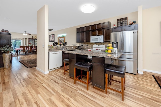 kitchen with white appliances, a kitchen breakfast bar, and light hardwood / wood-style flooring