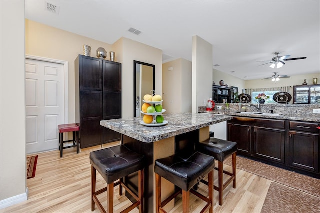 kitchen with sink, a kitchen breakfast bar, light stone counters, light hardwood / wood-style floors, and dark brown cabinets