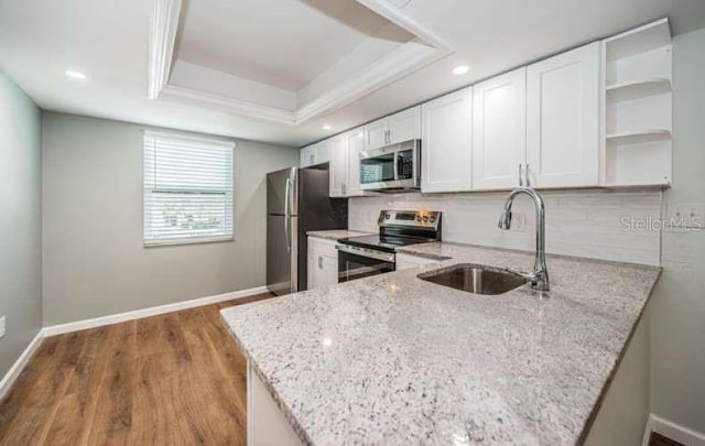 kitchen with stainless steel appliances, kitchen peninsula, sink, light stone countertops, and white cabinetry