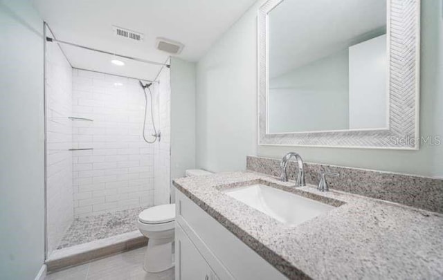 bathroom with toilet, vanity, tile patterned flooring, and a tile shower