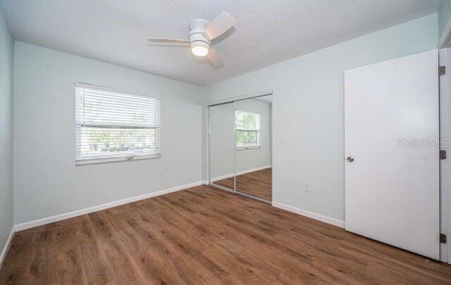 unfurnished bedroom with dark hardwood / wood-style floors, ceiling fan, multiple windows, and a closet